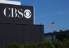 60 Minutes Veteran Walks Out—What Did Weiss Uncover? CBS sign on building, American flag in background.