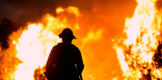 Firefighter silhouetted against massive wildfire flames