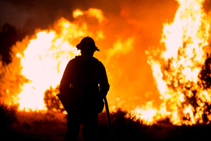 A,Firefighter,Watches,As,The,Bobcat,Fire,Burns,In,Juniper Firefighter silhouetted against massive wildfire flames