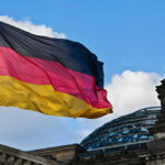 German flag waving against a blue sky near a historic building