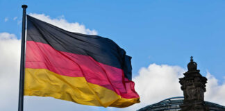 German flag waving against a blue sky near a historic building