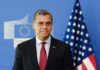 A political figure standing in front of European and American flags
