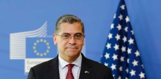 A political figure standing in front of European and American flags