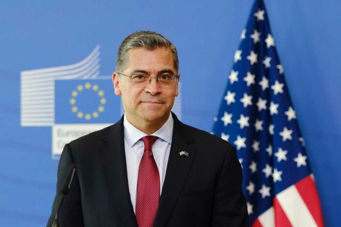 A political figure standing in front of European and American flags