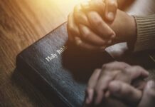 Prayer Event Funding Mystery: Taxpayer Dollars? Two hands clasped in prayer over a Holy Bible