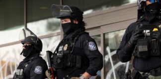 Three police officers in riot gear standing guard outside a building