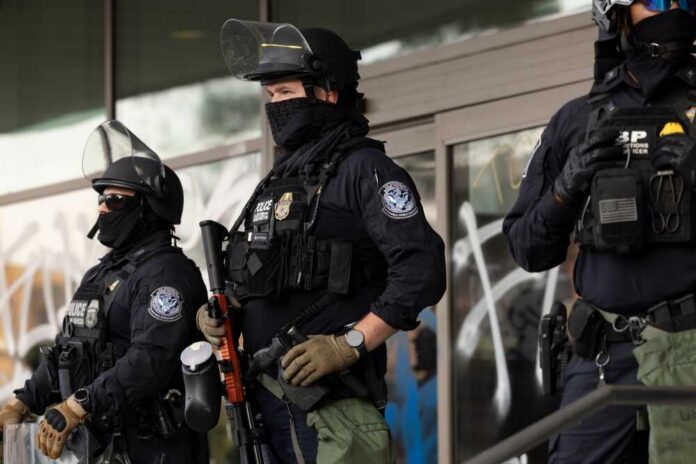 Three police officers in riot gear standing guard outside a building