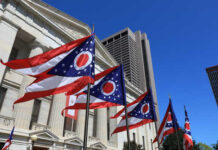 Ohio state flags waving in front of a government building under a clear blue sky