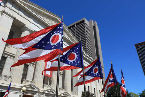 Ohio state flags waving in front of a government building under a clear blue sky