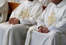 clergy in white vestments seated with hands folded