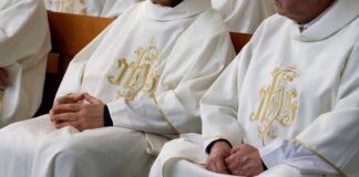 clergy in white vestments seated with hands folded