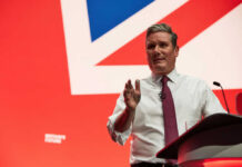 Man in white shirt and tie speaking at a podium on a red stage