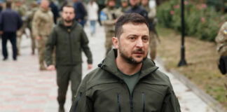 Zelensky walking outdoors with military personnel nearby.