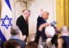Man speaking in front of Israeli flag backdrop