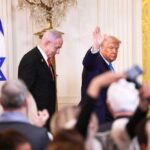Man speaking in front of Israeli flag backdrop