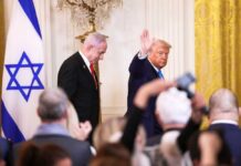 Man speaking in front of Israeli flag backdrop