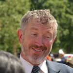 Taxpayer Gag Deals Revealed A smiling man in a suit engaging in conversation outdoors