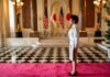 Japan Defense Moves Trigger China Backlash A woman in formal attire standing in a grand hall with flags in the background