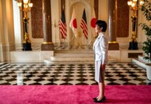 Japan Defense Moves Trigger China Backlash A woman in formal attire standing in a grand hall with flags in the background