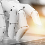 A robotic hand poised above a laptop keyboard