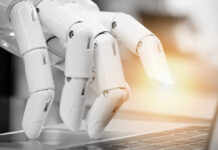 A robotic hand poised above a laptop keyboard