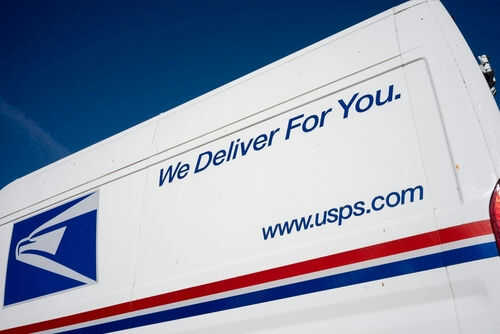 USPS delivery truck with logo and slogan visible