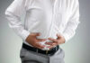 Elite Med Leader Trips On ‘Who Gets Pregnant’ Person clutching stomach in apparent discomfort.