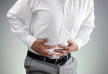 Elite Med Leader Trips On ‘Who Gets Pregnant’ Person clutching stomach in apparent discomfort.