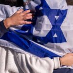 Ambassador Torches Khanna’s West Bank Tale People holding an Israeli flag together, showcasing unity and cultural pride