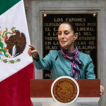Padded Victory? Mexico’s Murder Math War Person speaking at podium with Mexican flag nearby