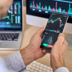 Broadcom Bombshell Rattles Wall Street Person checking stock market graphs on phone and monitors.
