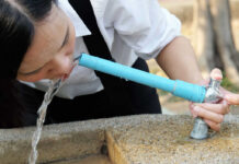 Poisoned Taps? Police Hunt Water Saboteur Person drinking water from a blue outdoor faucet