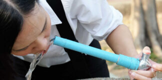 Person drinking water from a blue outdoor faucet