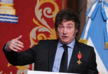 Man speaking with gestures, wearing a suit and medals.