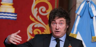 Man speaking with gestures, wearing a suit and medals.