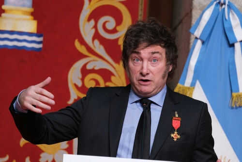 Man speaking with gestures, wearing a suit and medals.