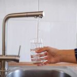Drought Emergency Triggers Island Rationing Hand filling a glass with water from a kitchen faucet