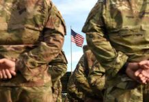 Fake VA Offer Sparks Identity Nightmares Soldiers in camouflage stand with hands behind backs facing a U.S. flag