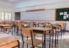 An empty classroom with wooden desks and a chalkboard