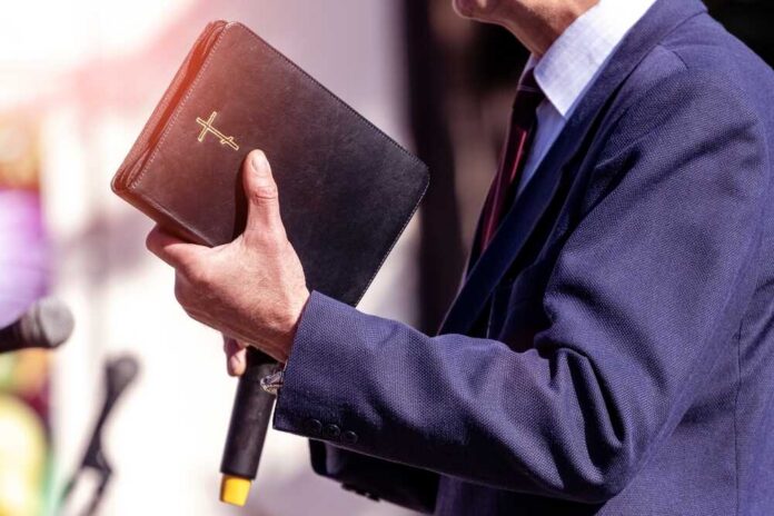 Pastor,With,A,Bible,In,His,Hand,During,A,Sermon. A person in formal attire holding a Bible while speaking