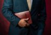 Person in a suit holding a red leather Bible