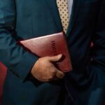 Person in a suit holding a red leather Bible