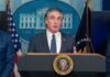 Government official speaking at a press conference in front of the White House seal