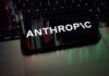 Trump Yanks AI Muzzle — Chaos Follows Smartphone displaying the word 'ANTHROPIC' over a background of financial graphs