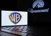 Hollywood Mega-Merger Ambushed by States Warner Bros logo displayed on a smartphone with Paramount logo in the background
