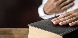 Hand on a thick black hardcover book on a wooden table