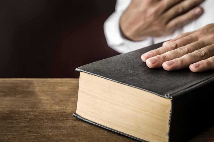 Hand on a thick black hardcover book on a wooden table