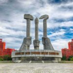 Monument with three raised stone hands holding hammer, sickle, and brush