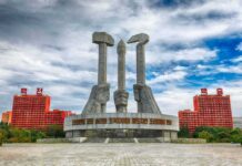 Nuke Boom Looms — Kim Goes Aggressive Monument with three raised stone hands holding hammer, sickle, and brush