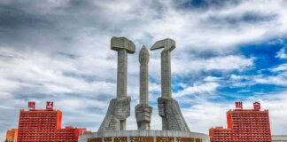 Monument with three raised stone hands holding hammer, sickle, and brush